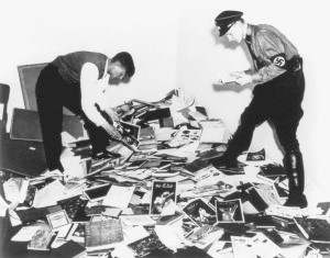 Zwei Studenten, rechts in SS-Uniform, durchsuchen einen zusammengesammelten Haufen von Dokumenten und Schriften aus dem Archivbestand des Berliner ›Instituts für Sexualwissenschaft‹.